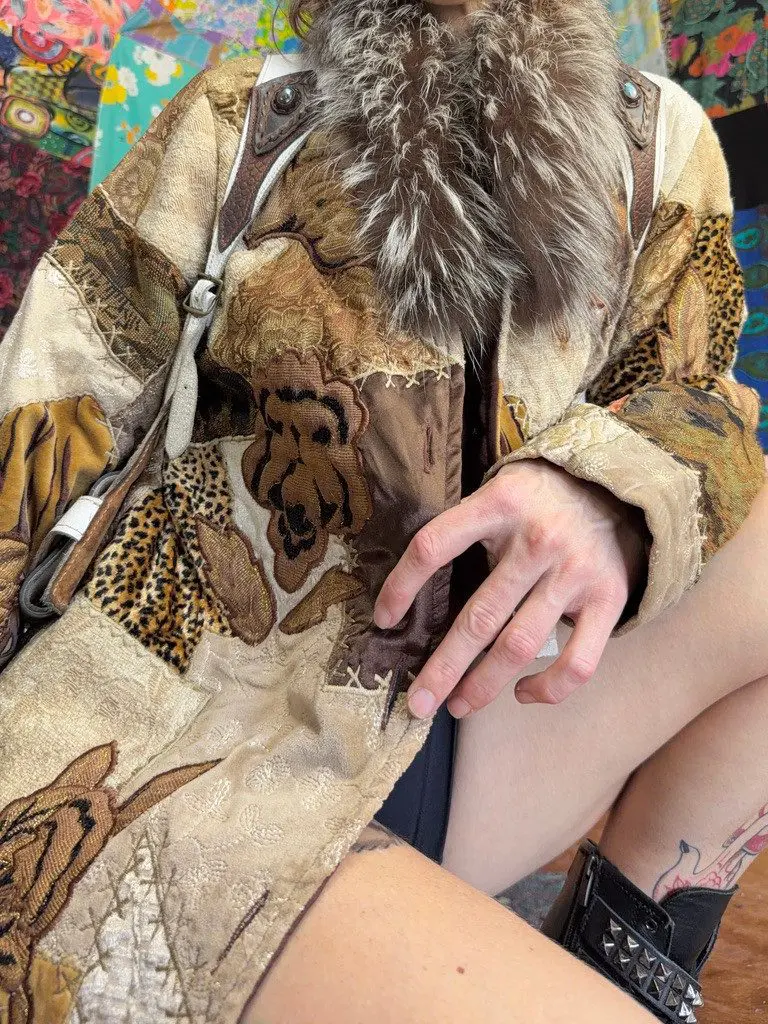 Seated person in ornate patchwork coat with fur