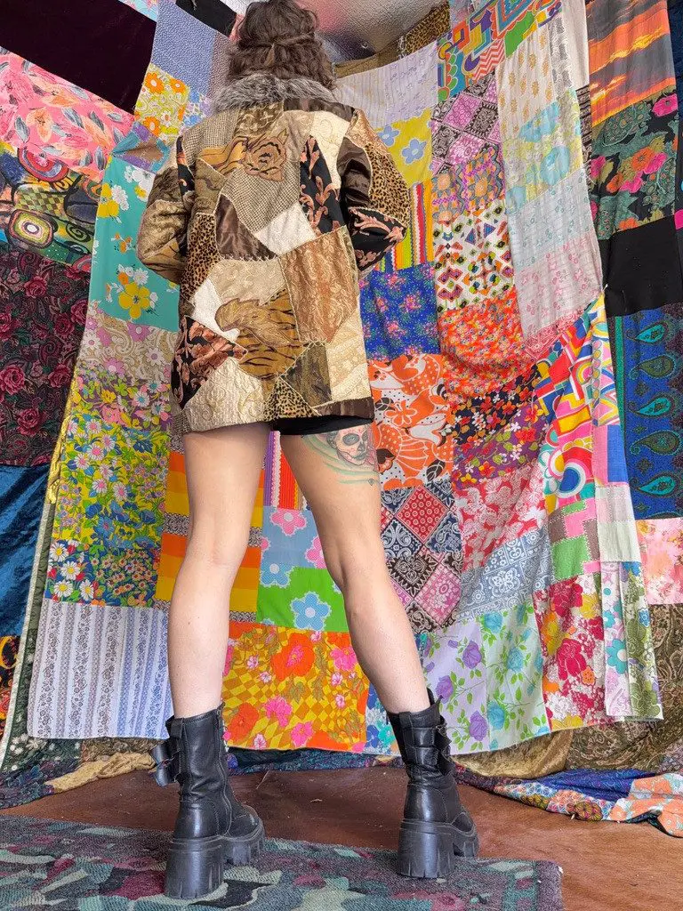 Person wearing patchwork jacket standing before colorful quilts